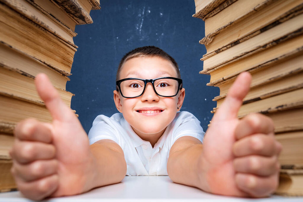 Smart boy in glasses sitting between two piles of books and look up thoughtfully - Foto, immagini