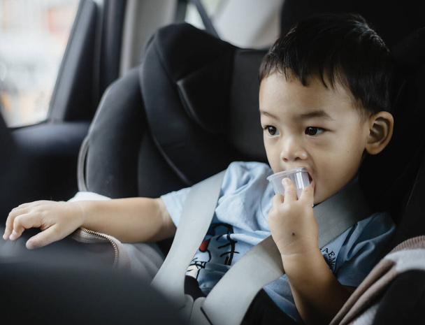 Ein Jahr alter entzückender asiatischer Junge, der sich allein im Autoporträt vom Autositz aus umsieht. Familienausflüge und Babybetreuung und Sicherheitskonzept. Vorderseite Headshot CloseUp Kopierraum und verschwommener Hintergrund. - Foto, Bild