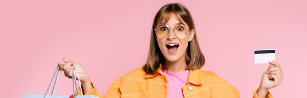 Podekscytowana młoda kobieta w okularach przeciwsłonecznych z kartą kredytową i torbami na zakupy na różowo  - Zdjęcie, obraz