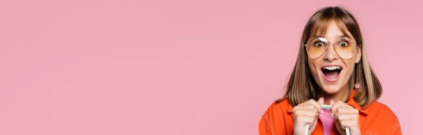 Panoramic shot of excited woman in sunglasses looking at camera isolated on pink - Фото, изображение