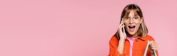 Panoramic shot of surprised woman in sunglasses looking at camera while talking on smartphone isolated on pink  - Fotoğraf, Görsel