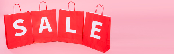 Οριζόντια καλλιέργεια πώληση λέξη σε κόκκινο τσάντες ψώνια σε ροζ φόντο - Φωτογραφία, εικόνα