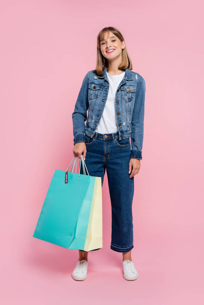 Young woman holding shopping bags with price tag and looking at camera on pink background - Photo, Image