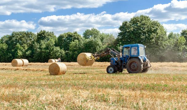 солома в круглых тюках и трактор в поле, сельскохозяйственные работы в летний день - Фото, изображение