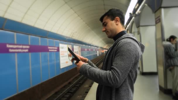 Человек использует планшет в метро. СМИ. Молодой человек пользуется планшетом в ожидании поезда в метро. Молодой человек ждет поезд метро с табличкой в руках - Кадры, видео