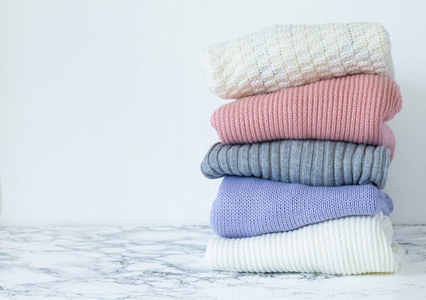 Stack of pastel color clothes. Pile of folded warm sweaters on marble table with space for your text - Foto, Imagen
