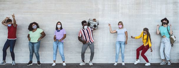 Happy friends wearing face mask listening music with vintage boombox outdoor - Multiracial young people having fun dancing together during corona virus outbreak - Youth millennial friendship concept - Photo, Image