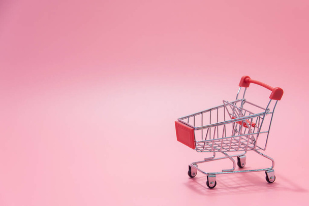 Concepto de compras - Carrito de compras rojo vacío sobre fondo rosa. los consumidores de compras en línea pueden comprar desde el hogar y el servicio de entrega. con spac de copia - Foto, imagen