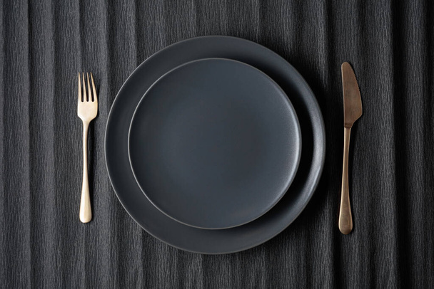 Пустые черные тарелки, вилка и нож на черном фоне. Вид сверху, пространство для копирования. - Фото, изображение