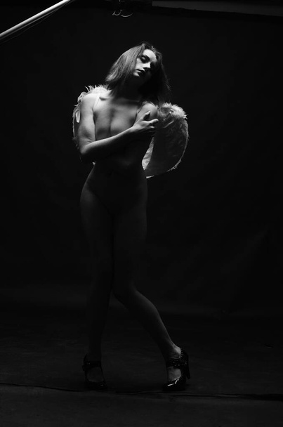 beautiful nude woman wearing decorative angel wings posing on dark background     - 写真・画像