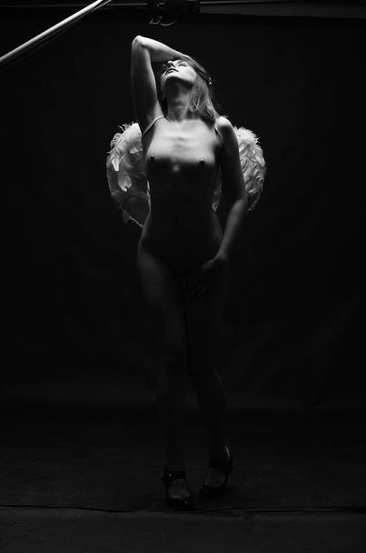 красивая обнаженная женщина в декоративных крыльях ангела позирует на темном фоне     - Фото, изображение