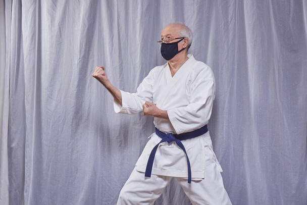 Oude atleet doet formele karate oefeningen in zelf-isolatie - Foto, afbeelding