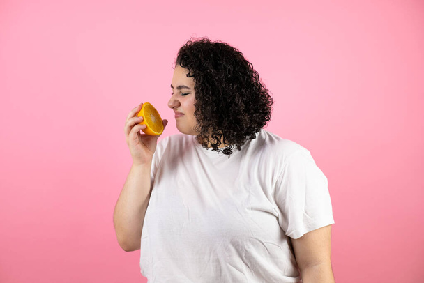 Young beautiful woman over isolated pink background disgusting expression and smelling a orange - Valokuva, kuva