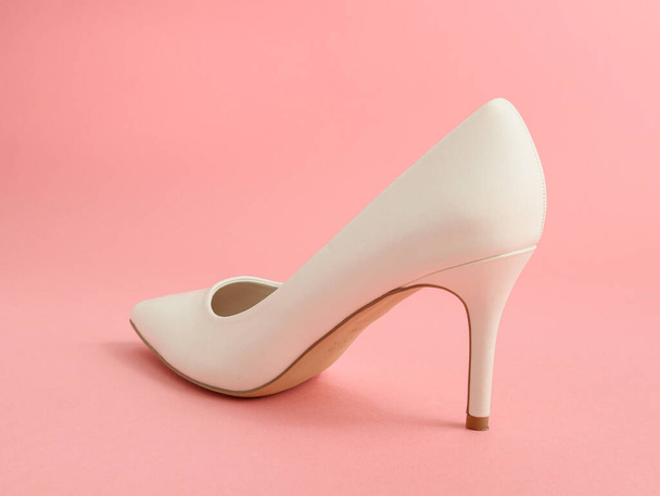 Een van de witte hoge hakken schoenen staat op een roze achtergrond, close-up zijaanzicht. - Foto, afbeelding