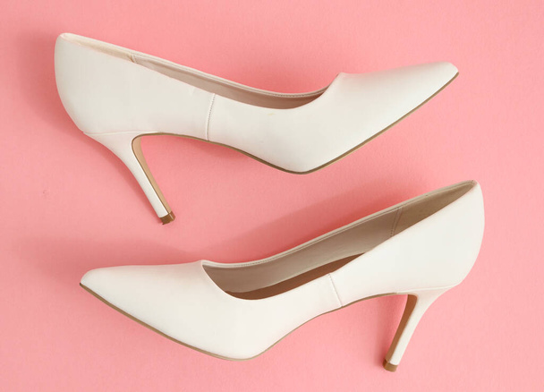 Ένα από τα λευκά ψηλοτάκουνα παπούτσια στέκεται σε ένα ροζ φόντο, κοντινό πλάνο πλευρά άποψη. - Φωτογραφία, εικόνα