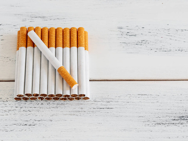 Cigarettes with an orange filter lying on the left on a white poharpone wooden table with space for text on the right. - Photo, Image