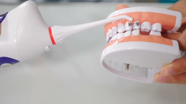 Mundhygiene für Zahnspangen. Kieferorthopädisches Behandlungskonzept. Lehre zur Zahnpflege. Zahnarzt zeigt, wie man Zähne mit dem Irrigator am Kiefermodell putzt. 4 k Video - Filmmaterial, Video