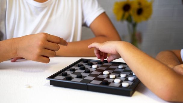 Дети играют в шашки на столе. Играет на шахматной доске в Черно-белой клетке. Досуг - Фото, изображение