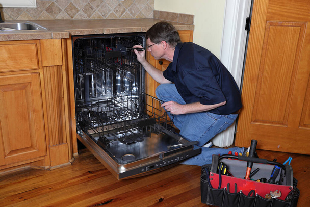 Alet tamir teknisyeni bozuk bulaşık makinesi üzerinde çalışıyor. - Fotoğraf, Görsel