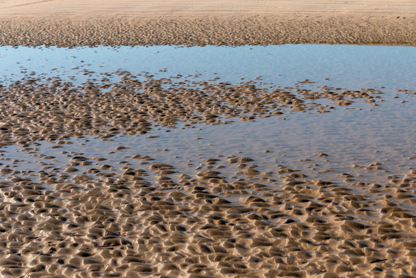 μια κοντινή άποψη των κυματισμών στην άμμο από τη χαμηλή παλίρροια με μια μικρή πισίνα νερού  - Φωτογραφία, εικόνα