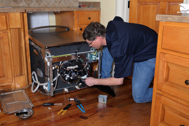 Техник по ремонту приборов работает над сломанной посудомоечной машиной - Фото, изображение