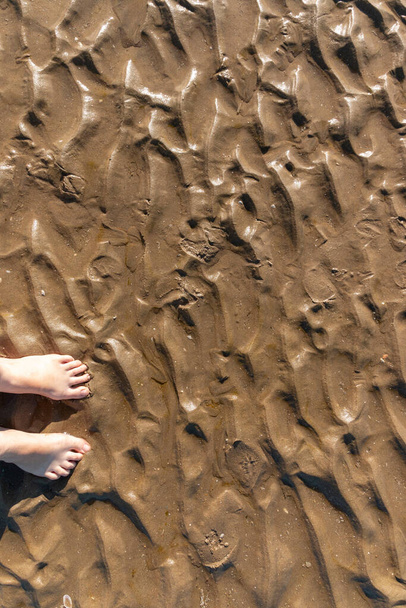een close-up zicht op de rimpelingen in het zand vanaf het laagwater met iemands voeten  - Foto, afbeelding