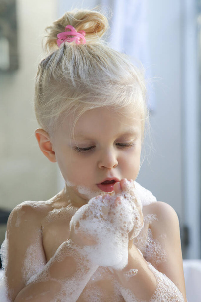 Rubia caucásica niña pequeña bañándose en una bañera llena de burbujas de jabón - Foto, imagen