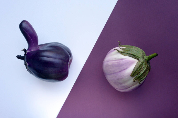Dwa brzydkie bakłażany na kontrastującym białym i fioletowym papierowym tle. Organiczne warzywo Solanum melongena. Świadoma koncepcja jedzenia. - Zdjęcie, obraz