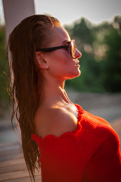 piękna brunetka modelka w czerwonym swetrze i ciemnych okularach przed kamerą. Zbliżenie i fotografowanie pełnowymiarowe. - Zdjęcie, obraz