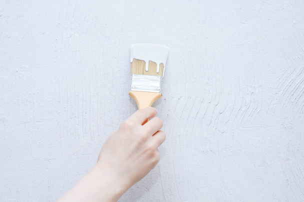 Home improvement. Hand of a Caucasian woman paints with a brush the wall with white paint. - 写真・画像