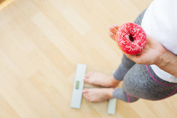 Concepto de dieta, la mujer mide el peso en balanzas electrónicas mientras sostiene la rosquilla de calorías - Foto, imagen