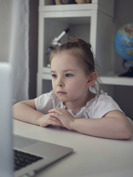 Evde dizüstü bilgisayar kullanan tatlı bir kız. Eğitim, online çalışma, evde öğrenim gören kız arkadaşlarıyla internet üzerinden iletişim kuruyor. Çocuklar uzaktan öğreniyor.  - Fotoğraf, Görsel