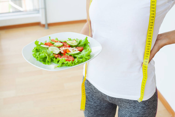 Diätfutter, Großaufnahme von frischem Salat in einer Schüssel und gelbem Maßband - Foto, Bild
