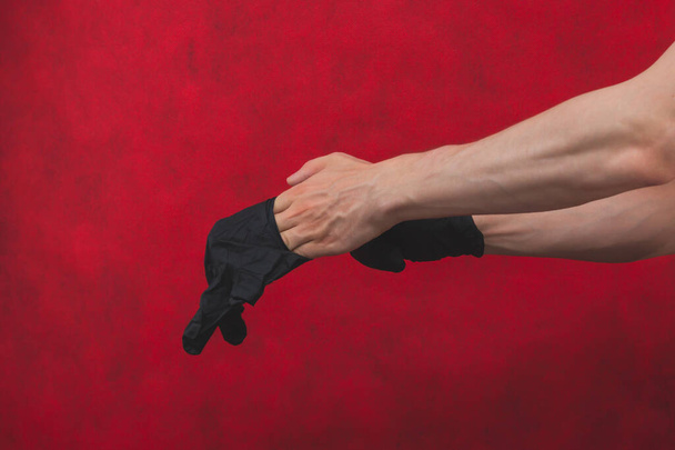 Hands in black medical gloves. person puts on surgical gloves on a red background - Foto, Imagem