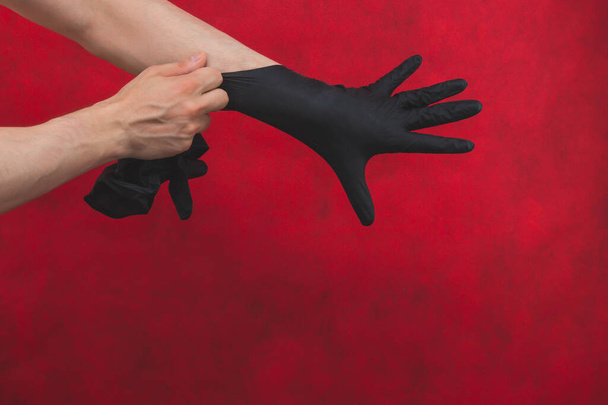 Hands in black medical gloves. person puts on surgical gloves on a red background - 写真・画像