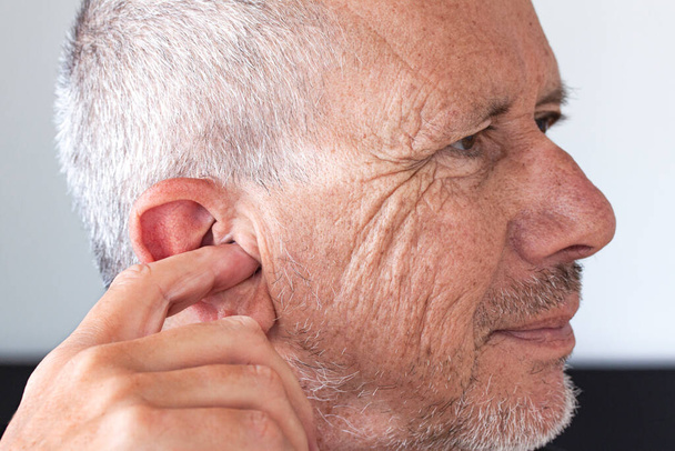 Starší muž s neoholeným strništěm a ukazováčkem se šťourá v uchu. Zavřít obrázek. - Fotografie, Obrázek