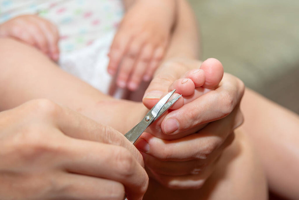 Mamá corta las uñas de los pies del bebé con pequeñas tijeras para bebés. Cuidado y tutela de los niños por parte de los padres - Foto, imagen