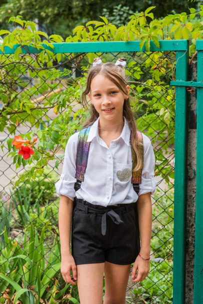 Okula yürümeye hazırlanan küçük bir kız. Okul üniformalı, sırt çantalı bir kız. Sonbaharda okul bahçesinde genç. - Fotoğraf, Görsel