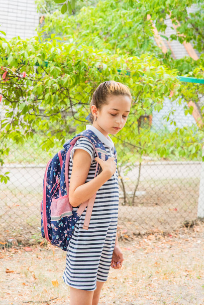 Una ragazzina che si prepara ad andare a scuola. Una ragazza in uniforme scolastica con uno zaino. Adolescente in autunno nel cortile della scuola - Foto, immagini