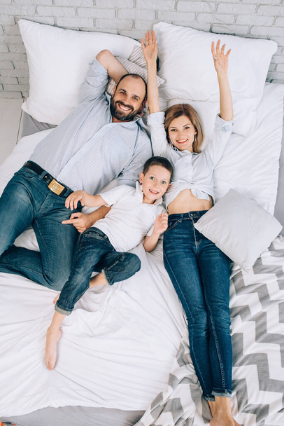 Caucasian cheerful family lies on a white bed. View from above. - Foto, Bild