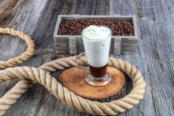 Caffe mocha with whipped cream. Latte macchiato in a tall glass. Glass of coffee latte and coffee beans on a dark background.  - Photo, Image