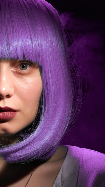 ritratto di una giovane ragazza con i capelli viola su uno sfondo nero con fumo viola. - Foto, immagini