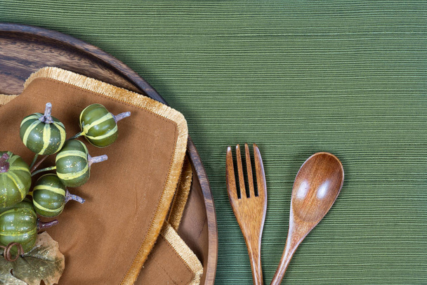 lieu avec assiette en bois, fourchette et cuillère sur une nappe verte avec serviette en or et décor vert - Photo, image