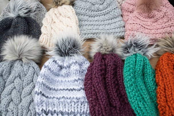 selection of hand crafted hats by knit or crochet with fake fur pom poms on a table for sale at a craft fair - Valokuva, kuva
