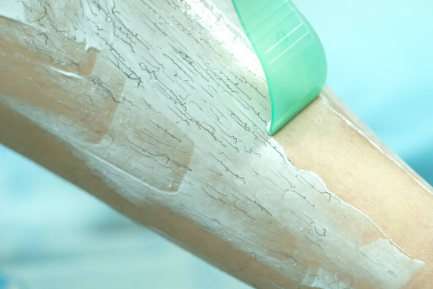 Γυναικείο πόδι αποτρίχωσης με κρέμα αποτρίχωσης και σπάτουλα. Καθαρίζει την κρέμα αποτρίχωσης - Φωτογραφία, εικόνα