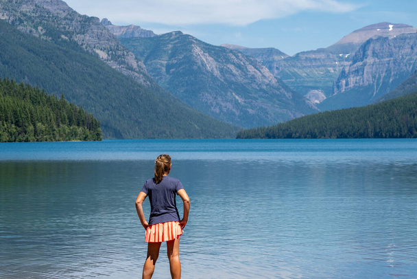 Attractive young woman with back facing camera looks at the scenery of Bowman Lake in Glacier National Park Montana - Photo, Image