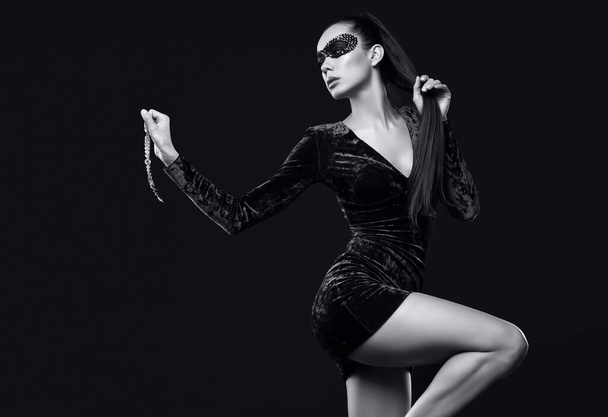 Retrato de encantadora mujer morena elegante en hermoso vestido púrpura y máscara de lentejuelas posando con collar de diamantes rojos sobre fondo negro en el estudio - Foto, imagen