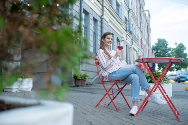 Smiling female sitting with crossed legs, enjoying red wine in cafe - Fotó, kép