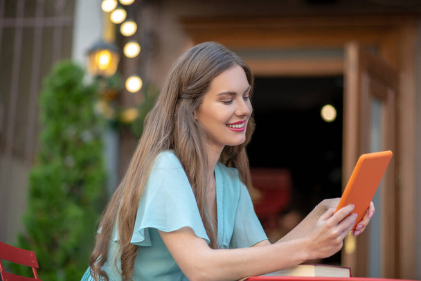 Romantic female sitting in open air cafe, holding orange tablet - 写真・画像