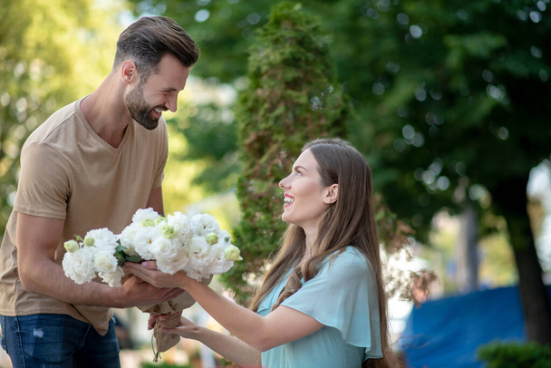 Bearded male presenting bouquet of white flowers to pretty female - Photo, Image